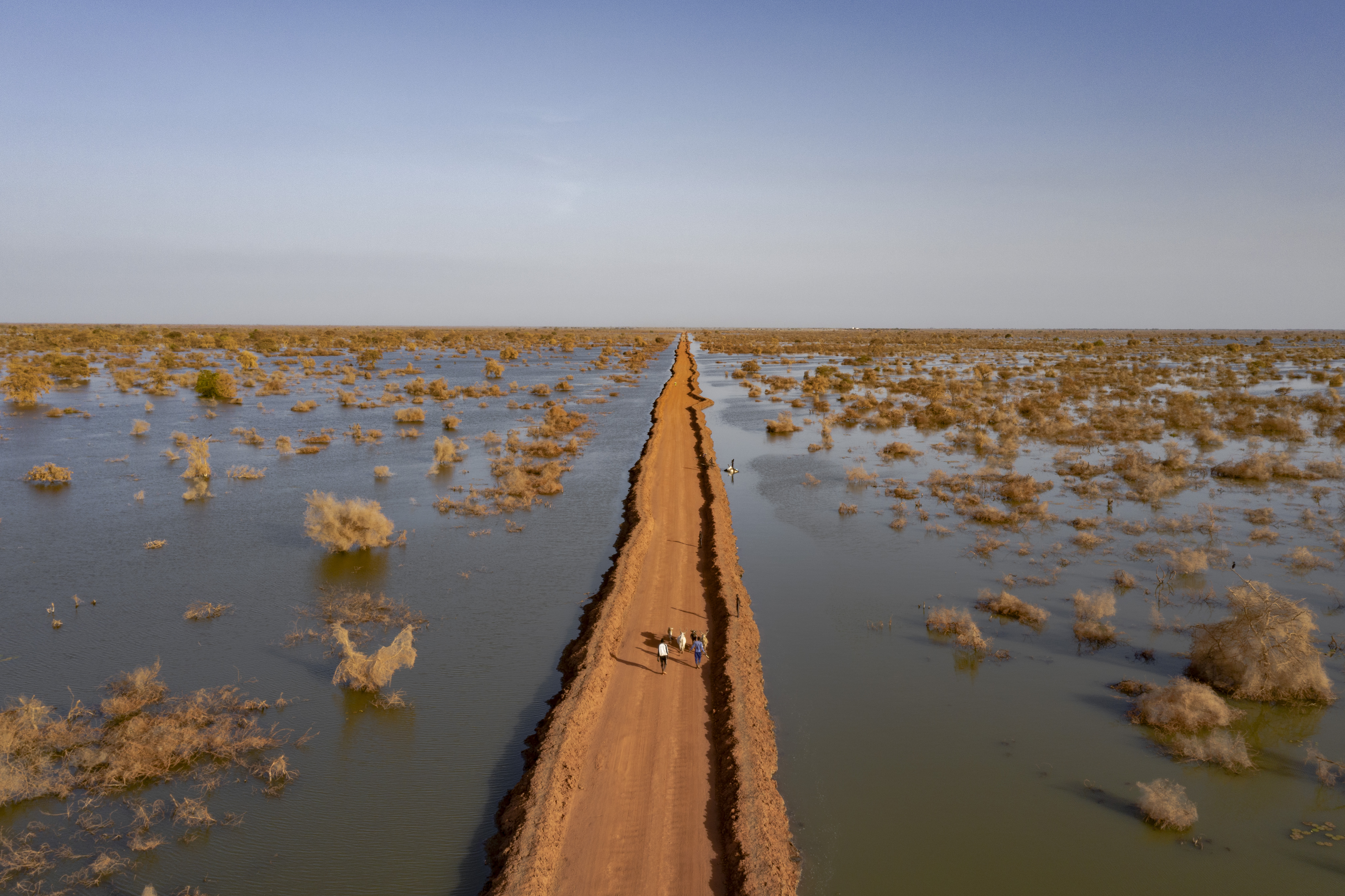 Pessoas caminham ao longo de uma estrada protegida por diques através das águas das cheias perto de Benitu, no Sudão do Sul. © UNHCR/Andrew McConnell